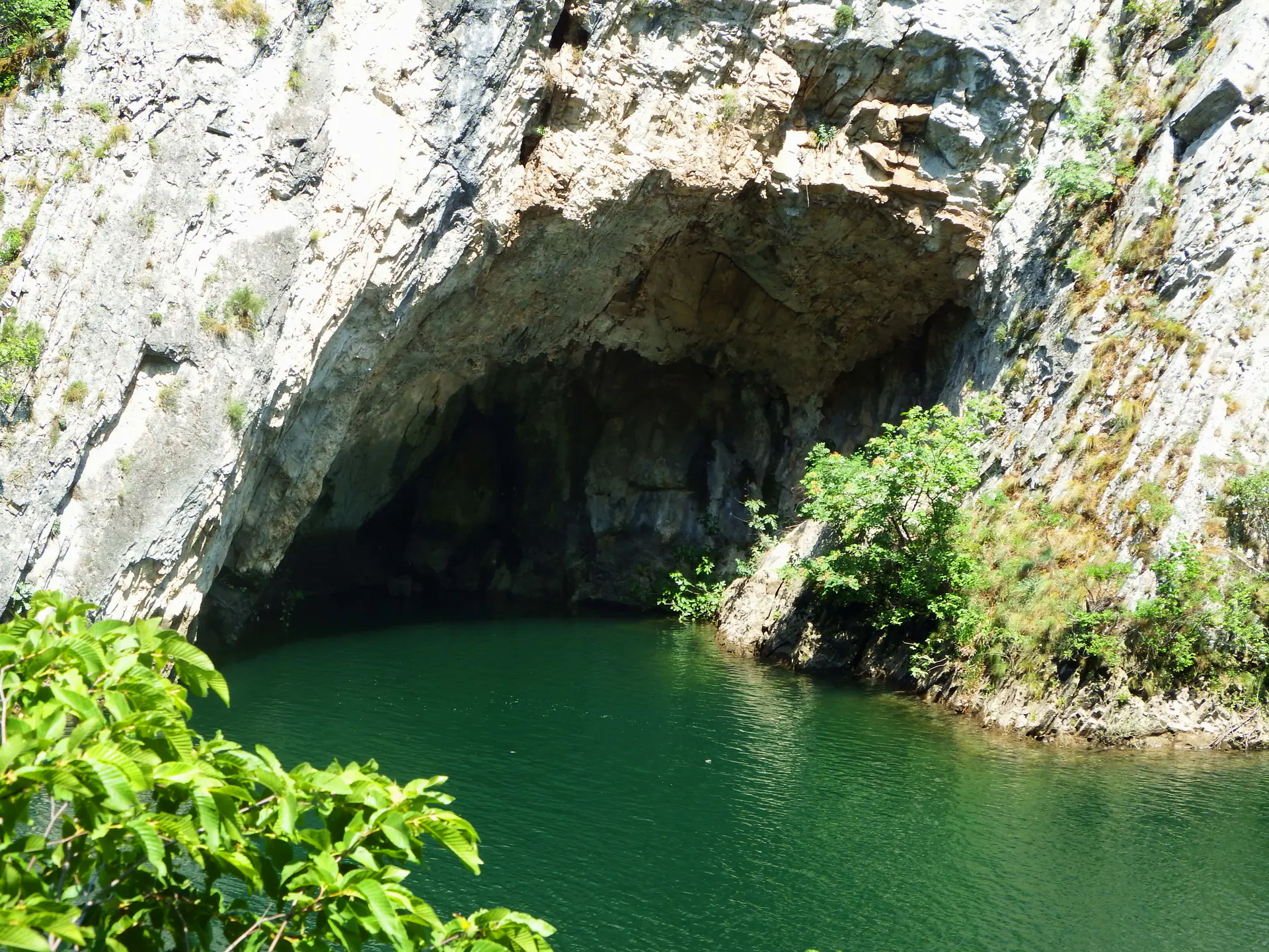A cave opening meeting green water between the cliffs of Matka Canyon